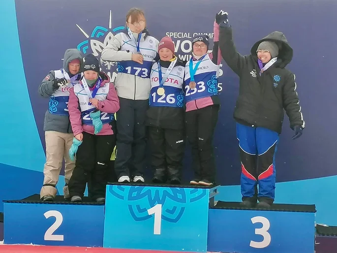 Eine Gruppe von Menschen auf einem Podium, die stolz ihre Medaillen präsentieren.