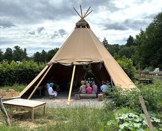 Kinder sitzen im halb geöffneten Tipi des Naturkindergartens Wald- und Wiesenwichtel