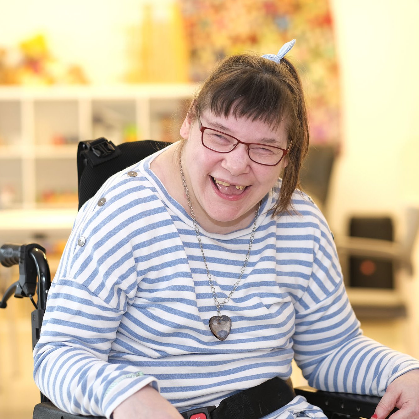 Eine Frau mit mehrfacher Behinderung in einem Rollstuhl lacht.
