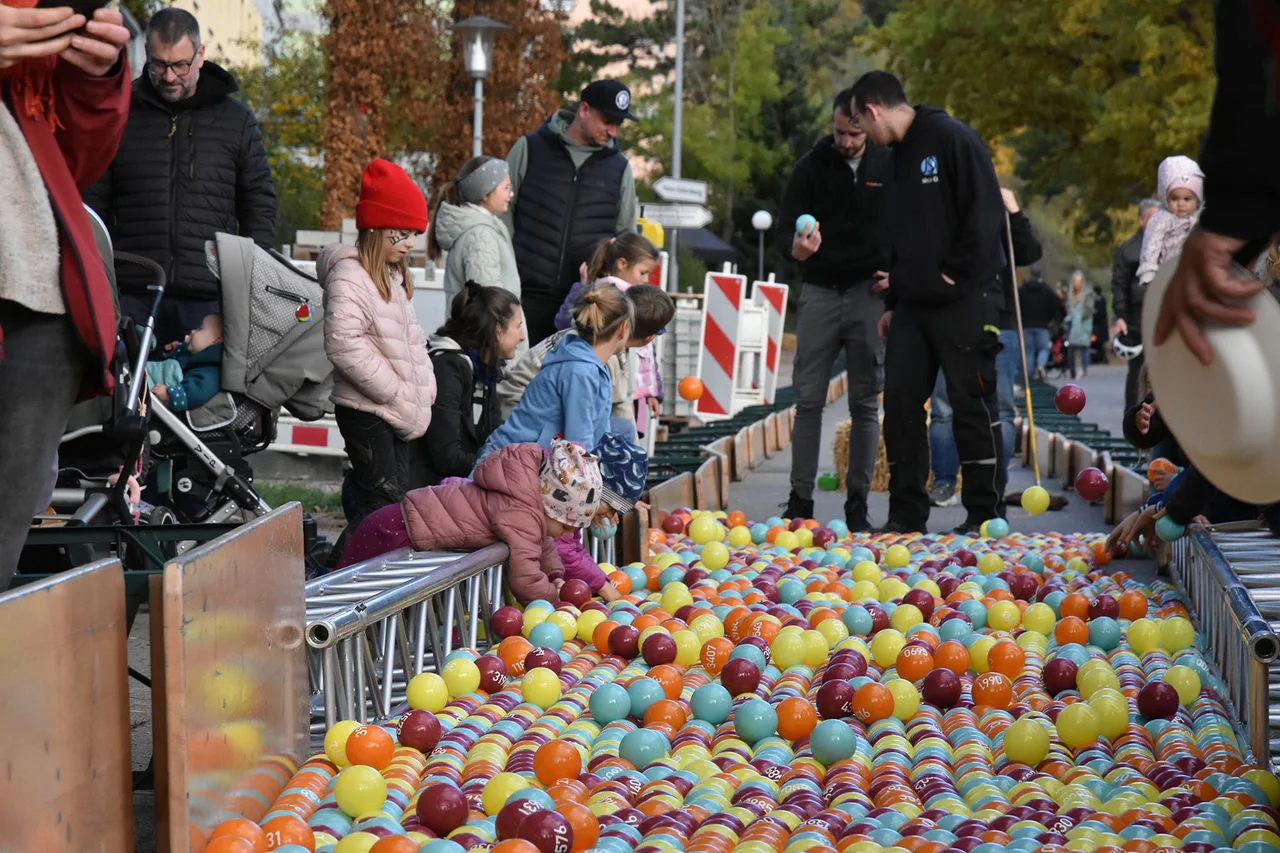 Menschen stehen an Banden und schauen auf sehr viele bunte Bälle, die ins Ziel kommen.