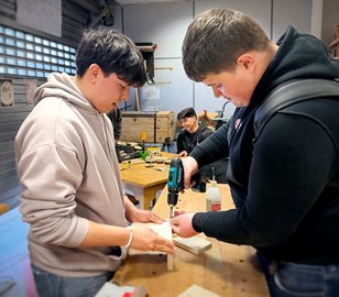 Zwei Auszubildende arbeiten an einer Holz-Werkbank.