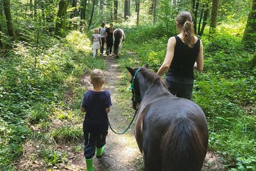 Kinder und Betreuerinnen führen Pferde durch den Wald.