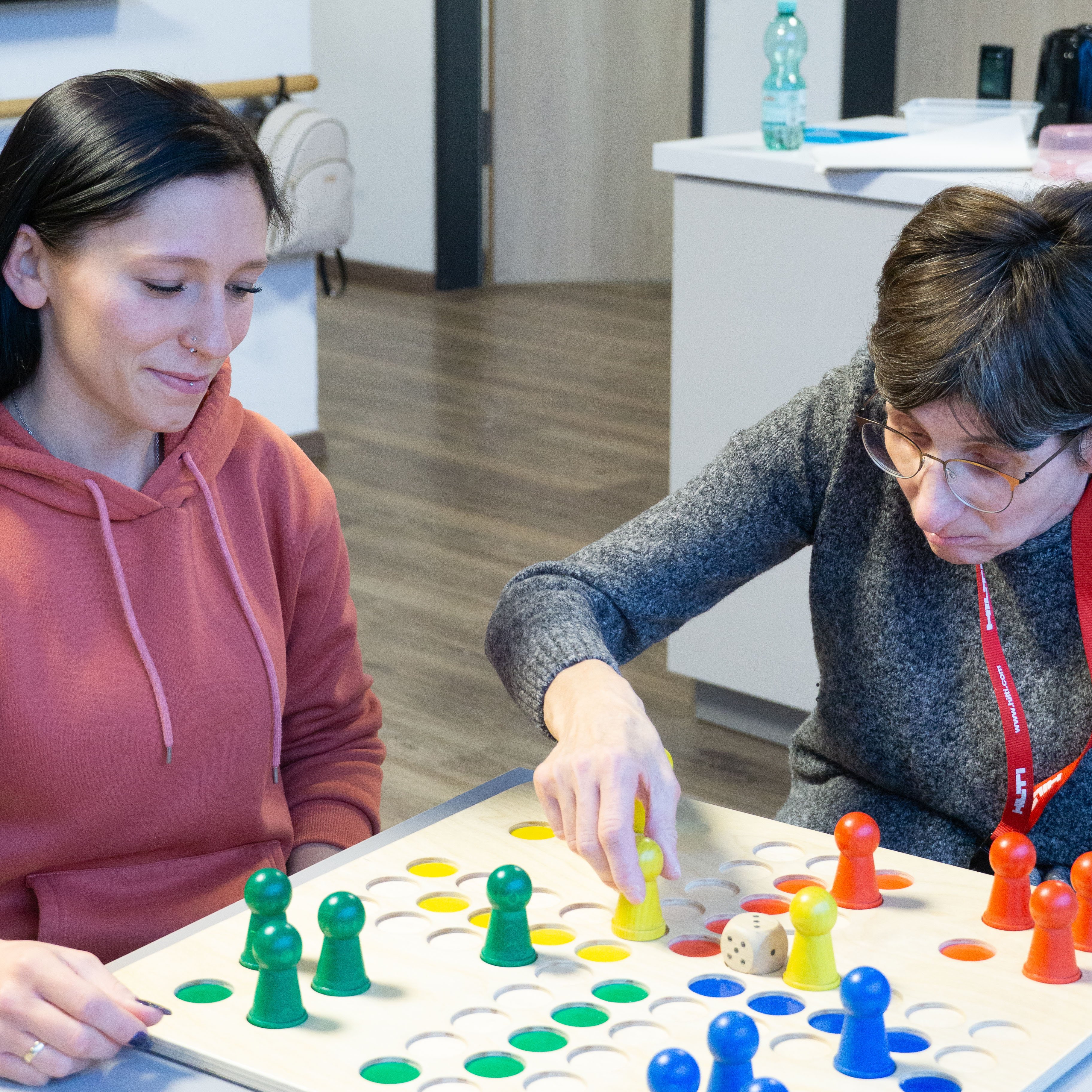 Eine Mitarbeiterin und eine Klientin spielen zusammen ein Brettspiel.
