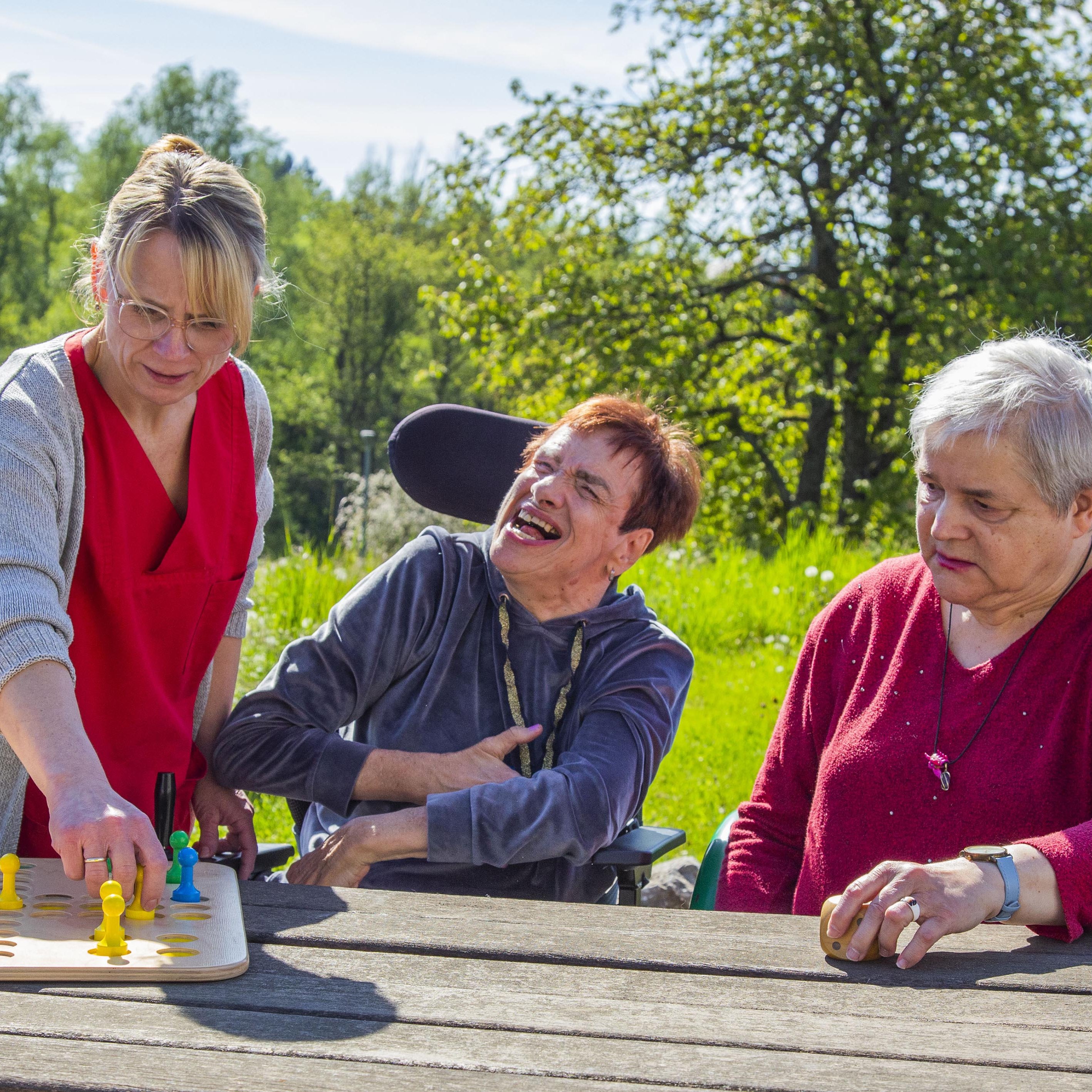 Drei Frauen an einem Tisch, eine Frau steht, die anderen sitzen und sie spielen ein Spiel.