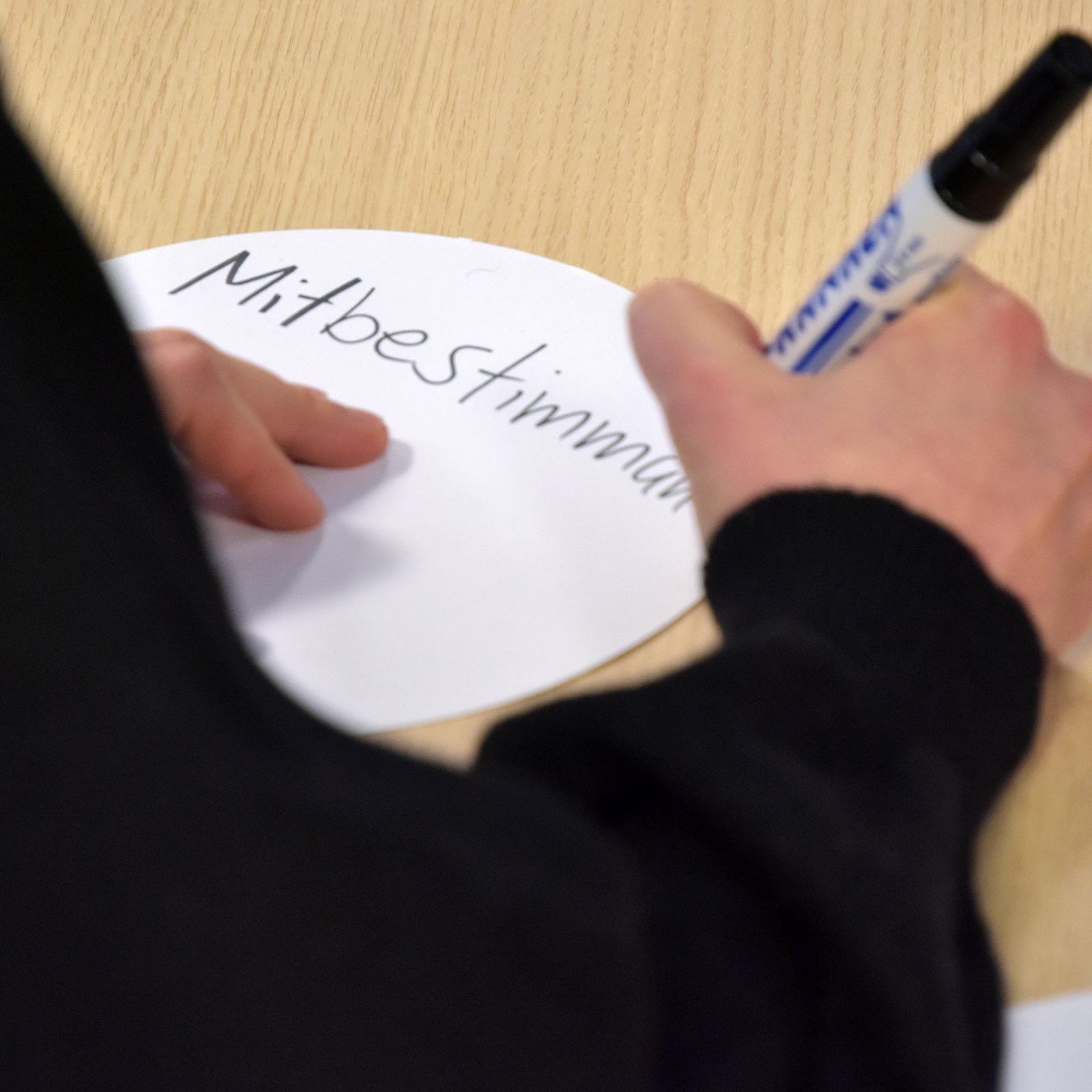 Eine Person schreibt "Mitbestimmung" auf ein Stück Papier.