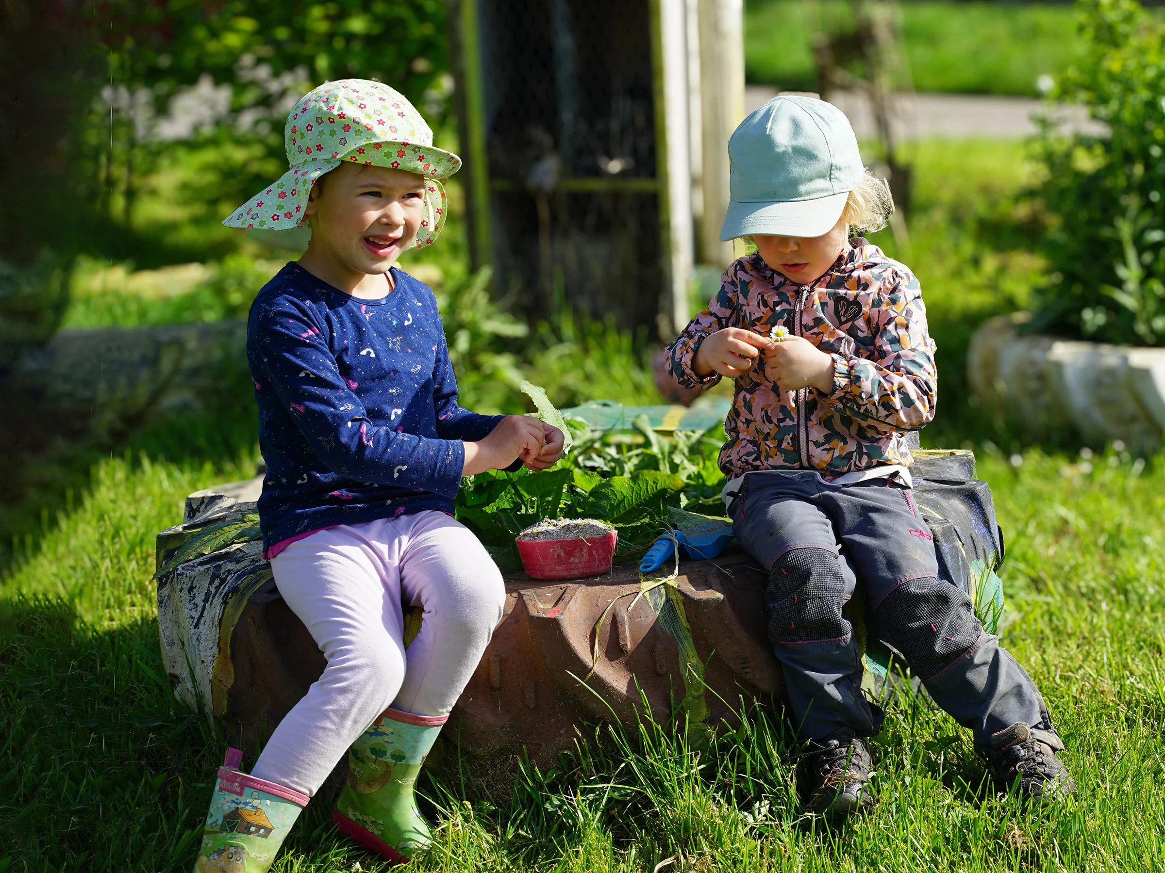 Zwei Kinder sitzen im Garten in der Sonne.