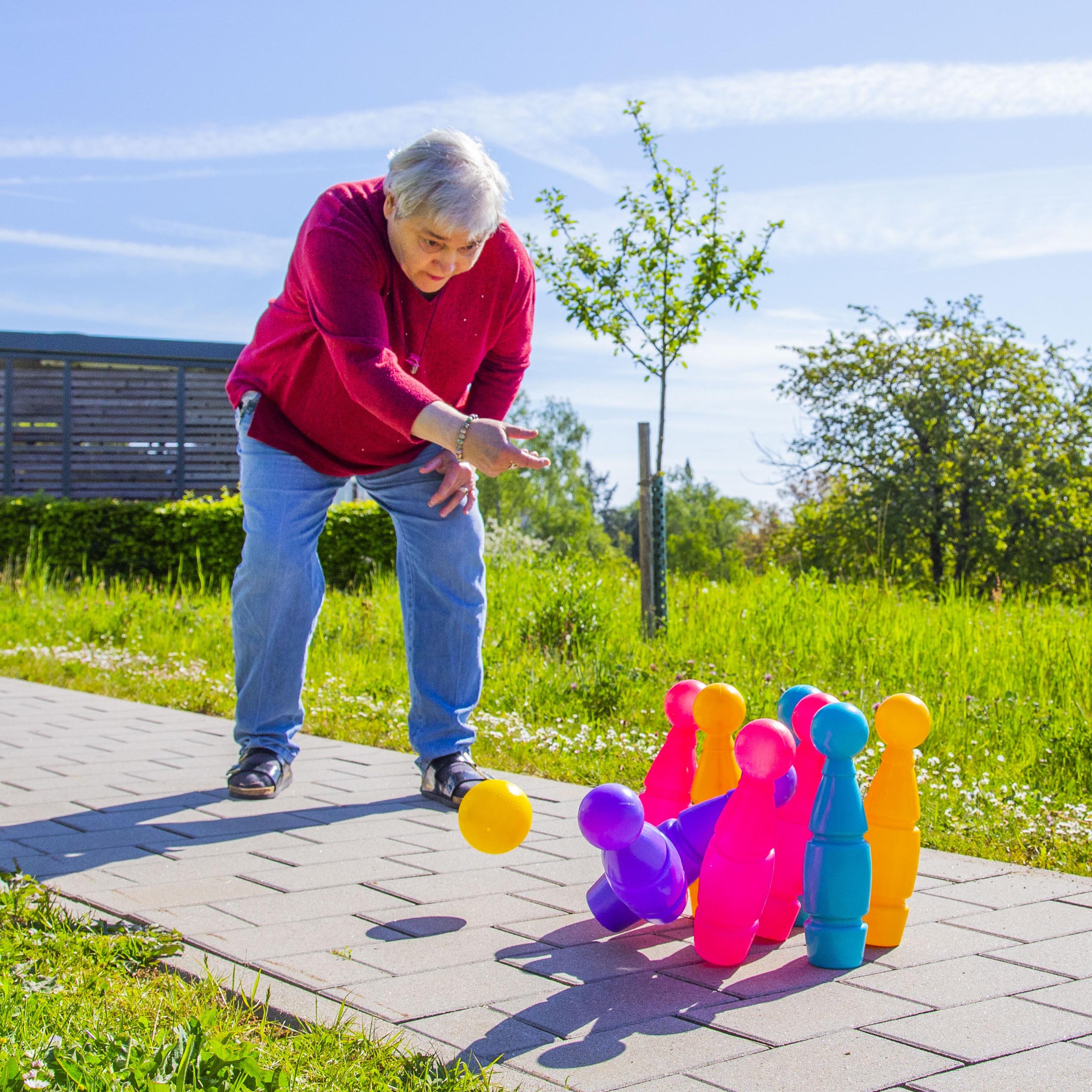 Eine Frau wirft einen Ball auf vor ihr stehende bunte Kegel.