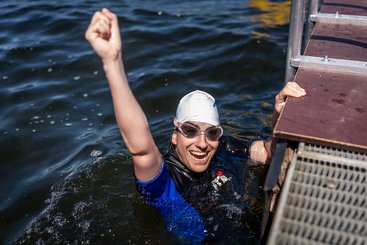 Eine Frau in einem Neoprenanzug und mit Schwimmbrille schaut aus dem Wasser und jubelt.