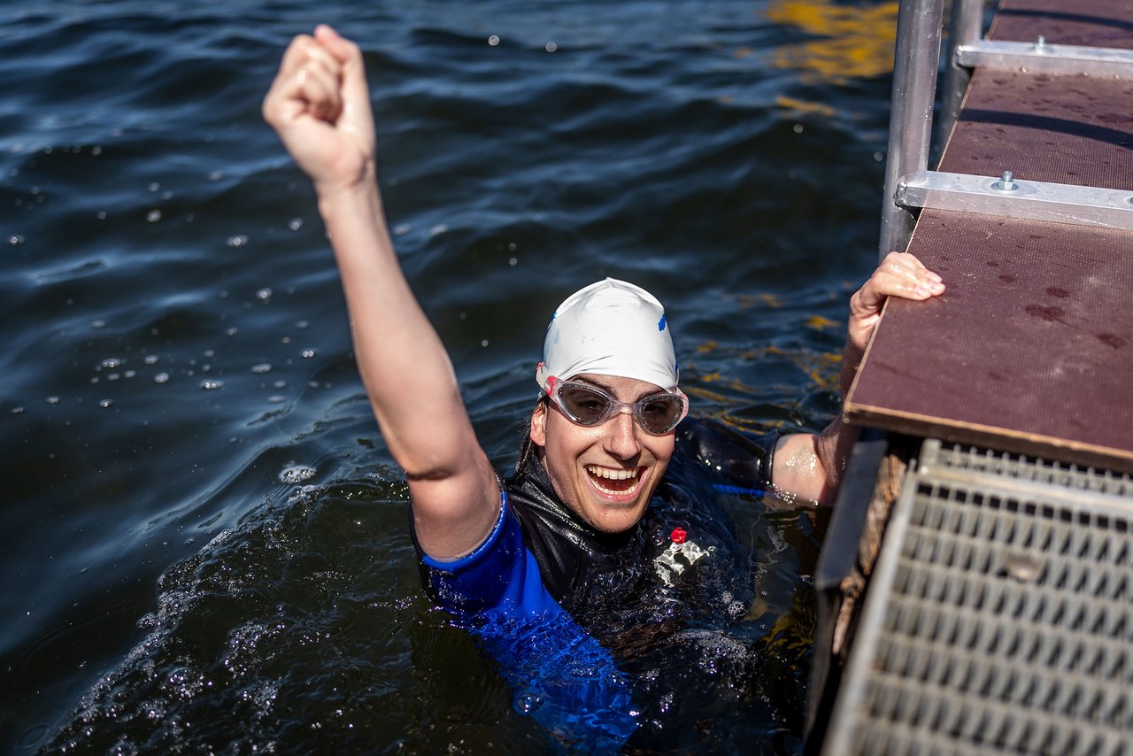 Eine Frau in einem Neoprenanzug und mit Schwimmbrille schaut aus dem Wasser und jubelt.