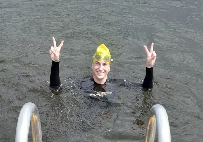 Eine Schwimmerin schaut mit dem Kopf aus dem Wasser, lacht und zeigt mit beiden Händen das Victory-Zeichen.