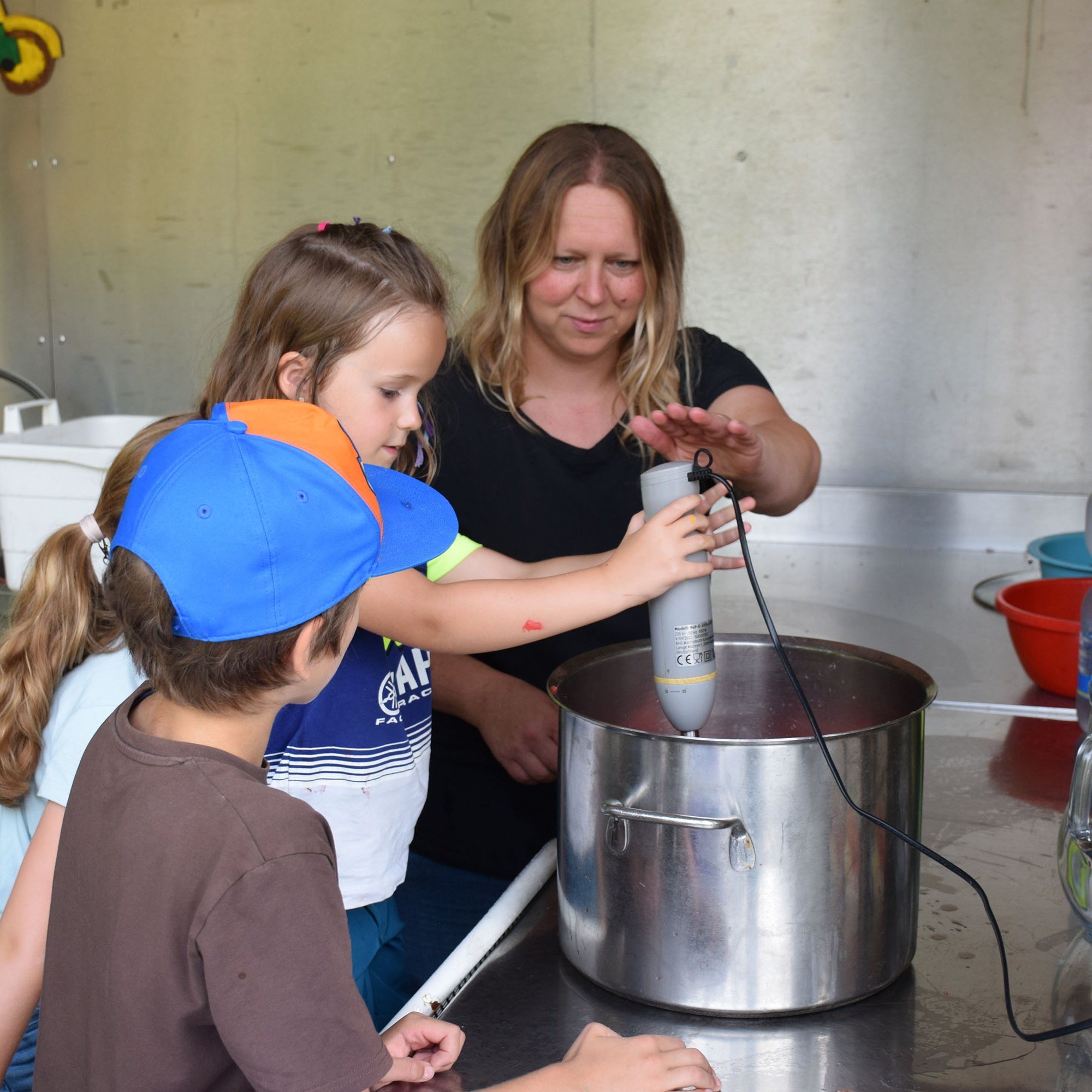 Eine Frau und drei Kinder rühren in einem großen Topf.