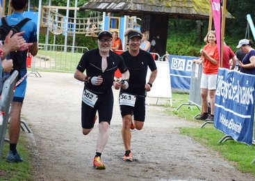 Zwei Männer laufen in einem Triathlon-Rennen, lächelnd und in sportlicher Kleidung.