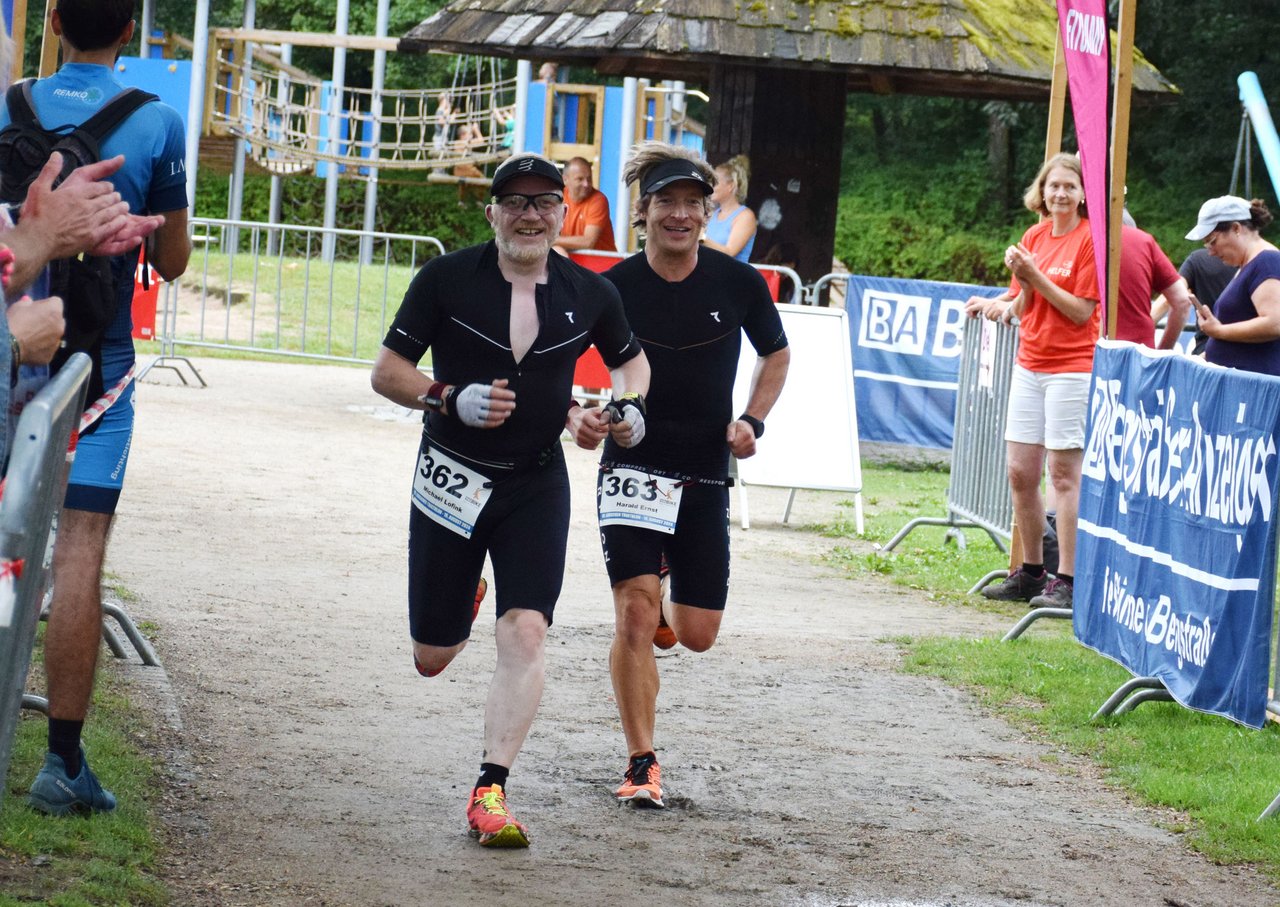 Zwei Männer laufen in einem Triathlon-Rennen, lächelnd und in sportlicher Kleidung.