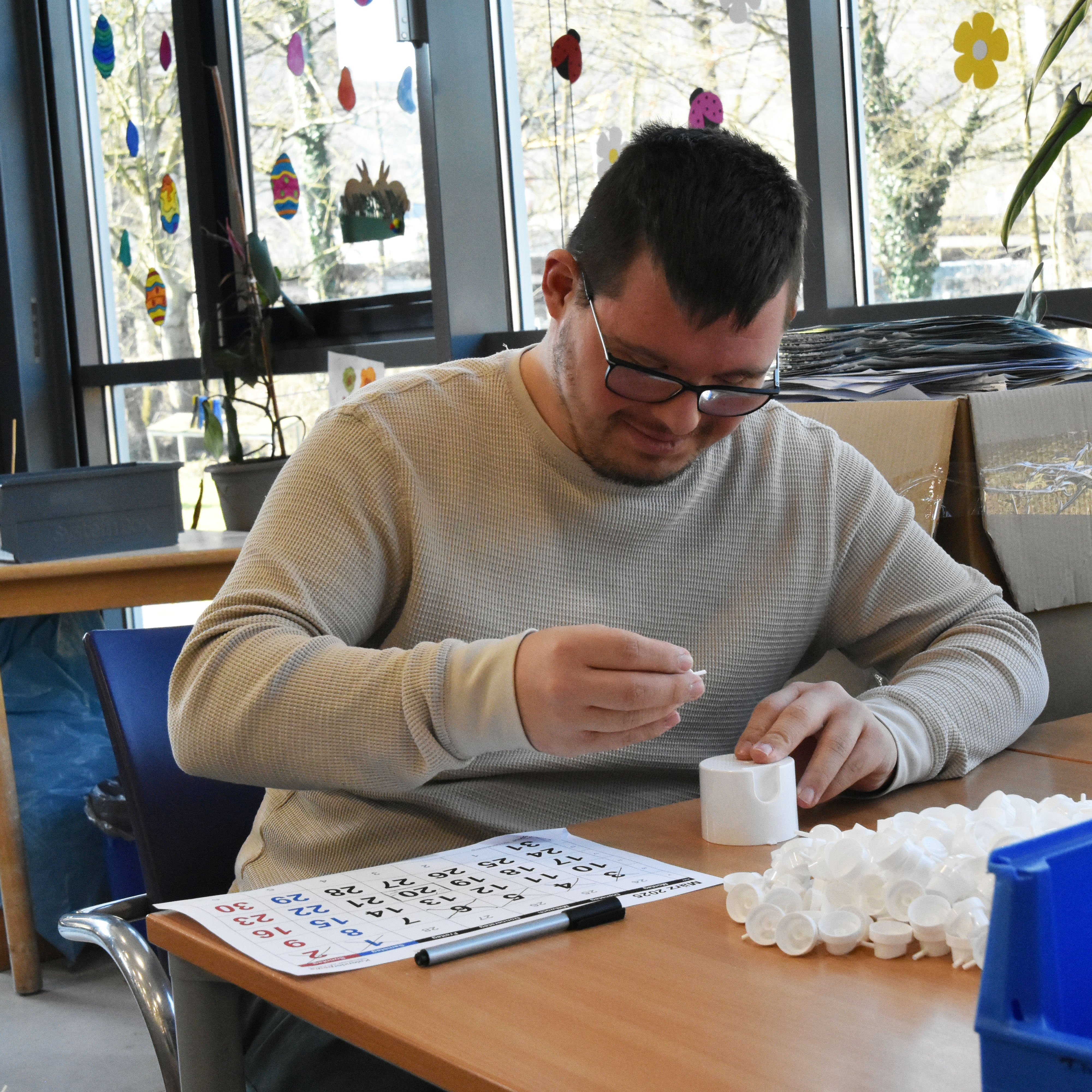 Ein Mann sitzt an einem Tisch und baut weiße Teile aus Plastik zusammen.