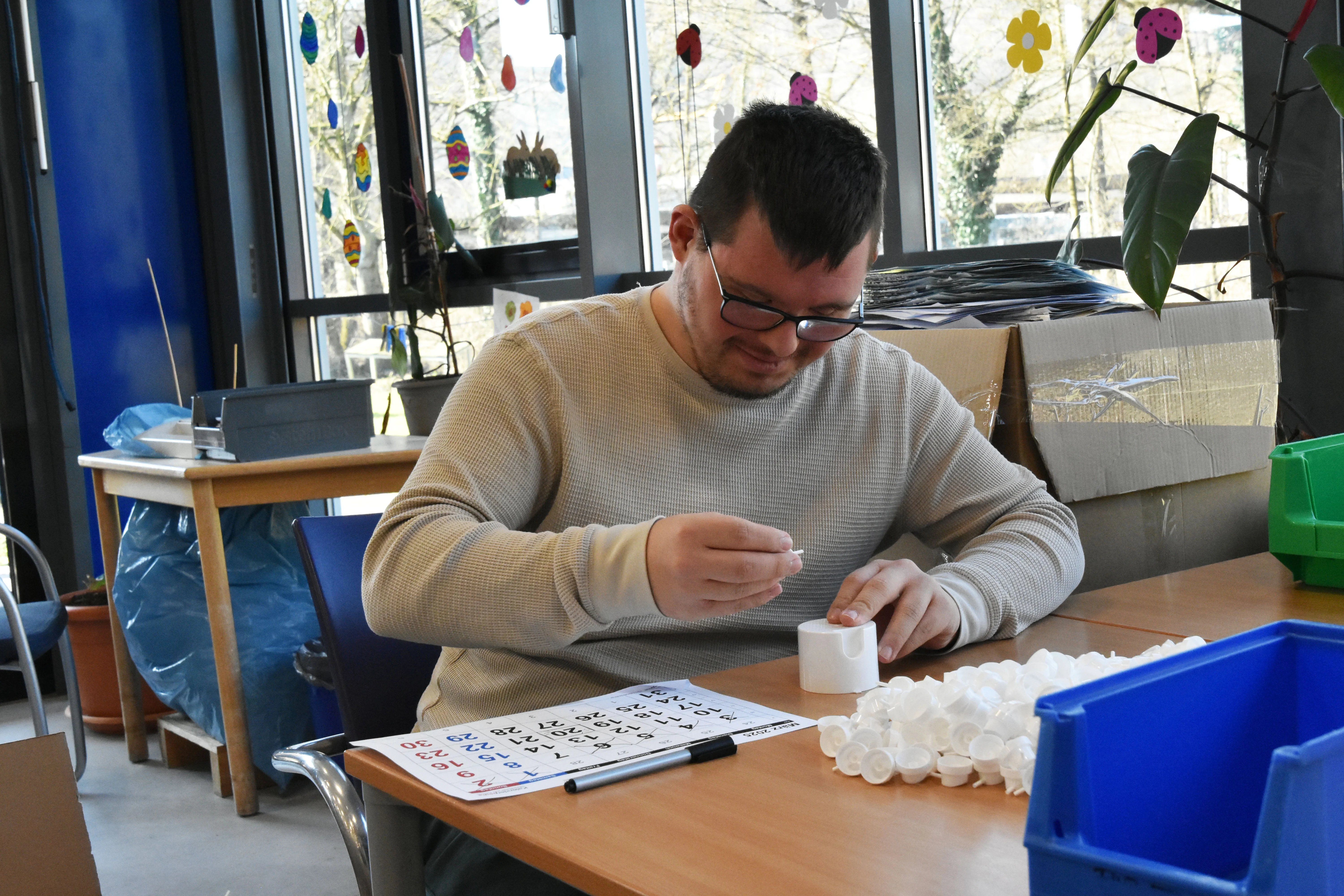 Ein Mann sitzt an einem Tisch und baut weiße Teile aus Plastik zusammen.