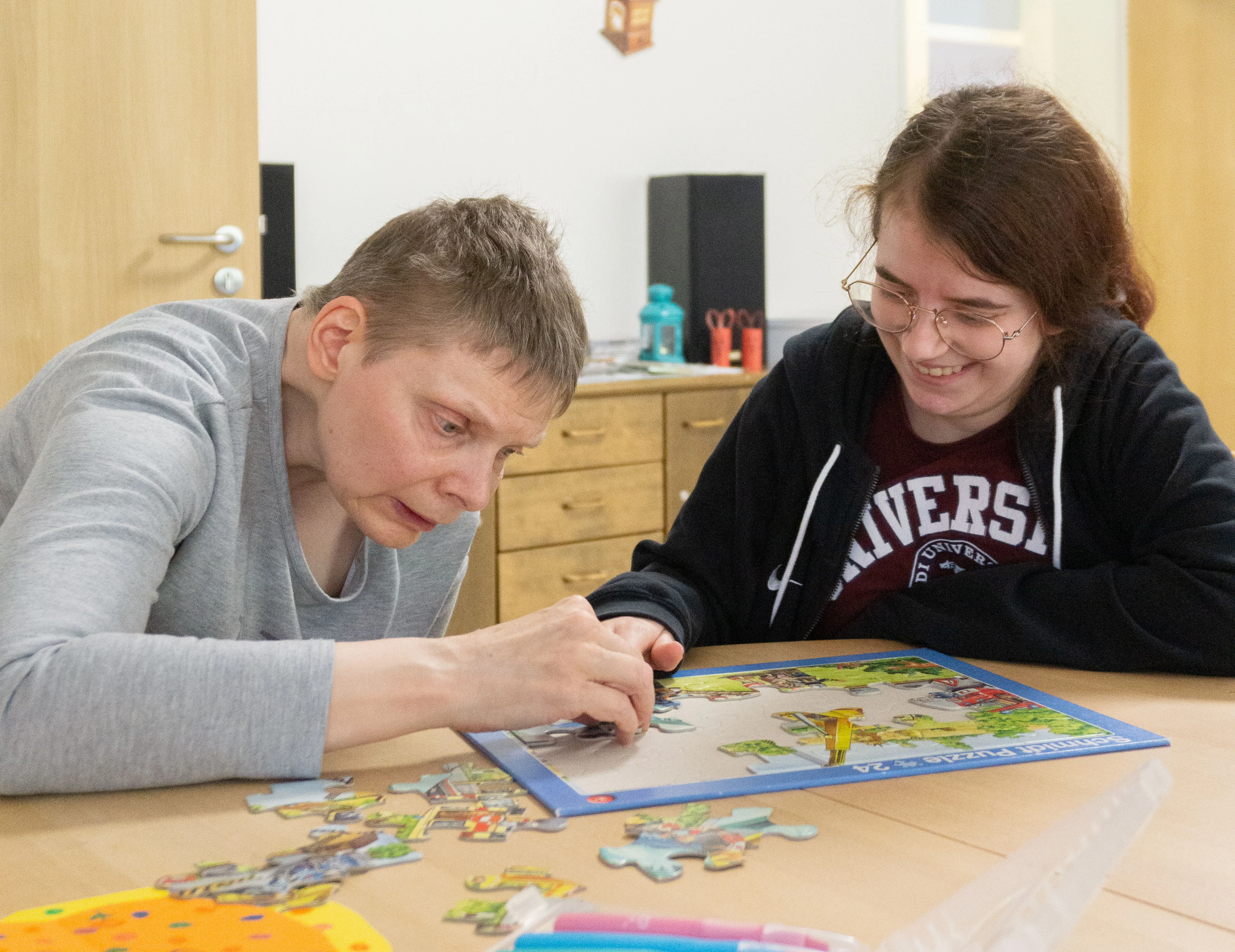 Eine junge Mitarbeiterin puzzelt zusammen mit einer älteren Klientin.