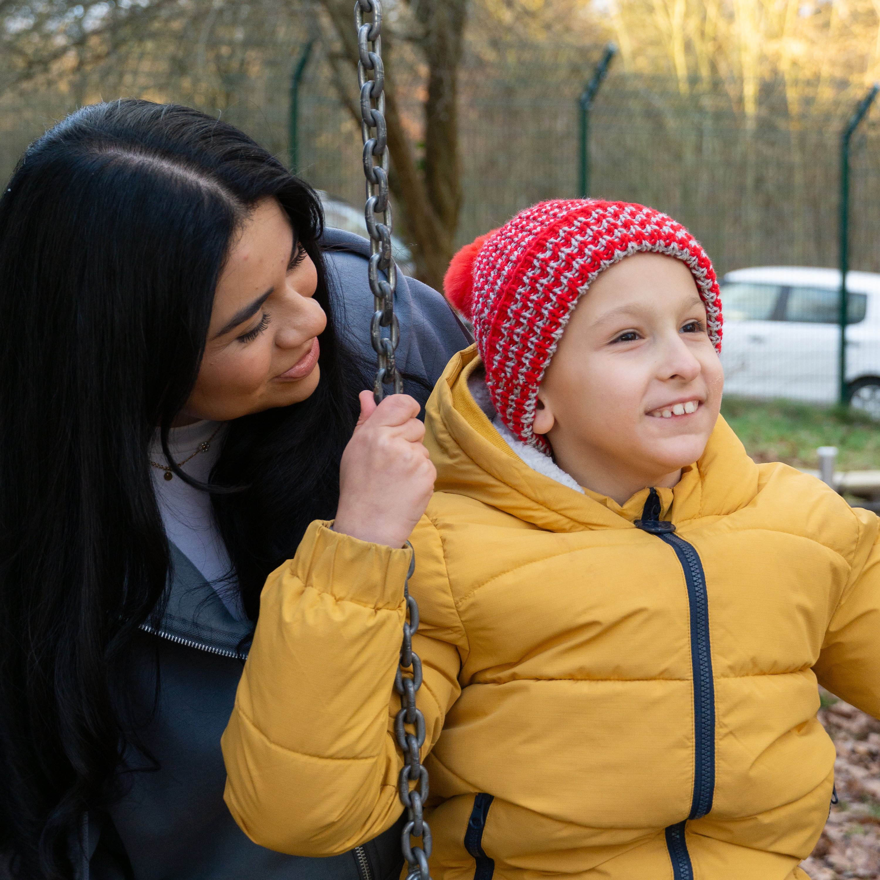 Eine Mitarbeiterin beugt sich zu einem Jungen, der auf einer Schaukel sitzt.