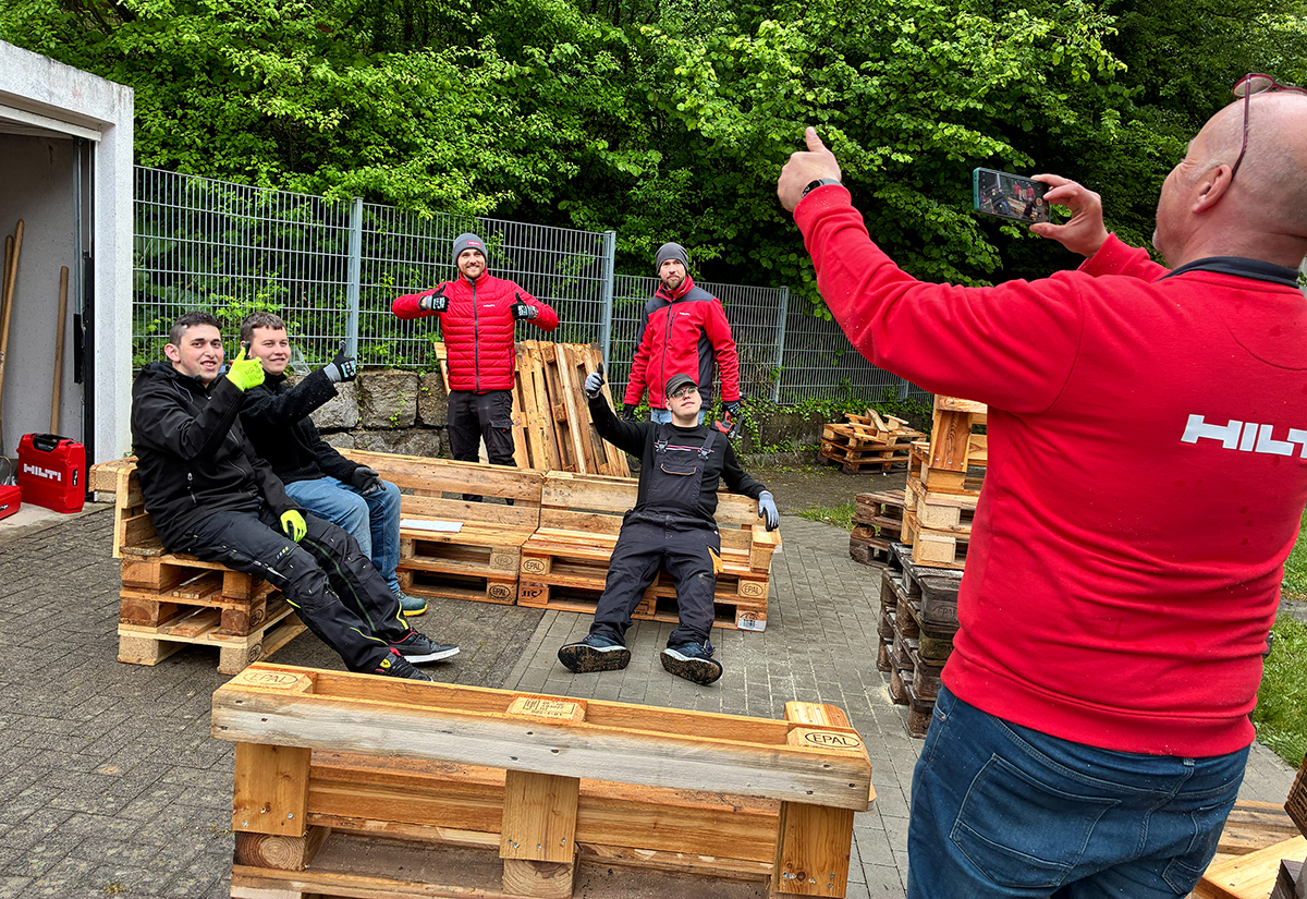 Ein Hilti-Mitarbeiter macht Fotos von Kollegen und Schülern, die auf Palettenmöbeln sitzen.