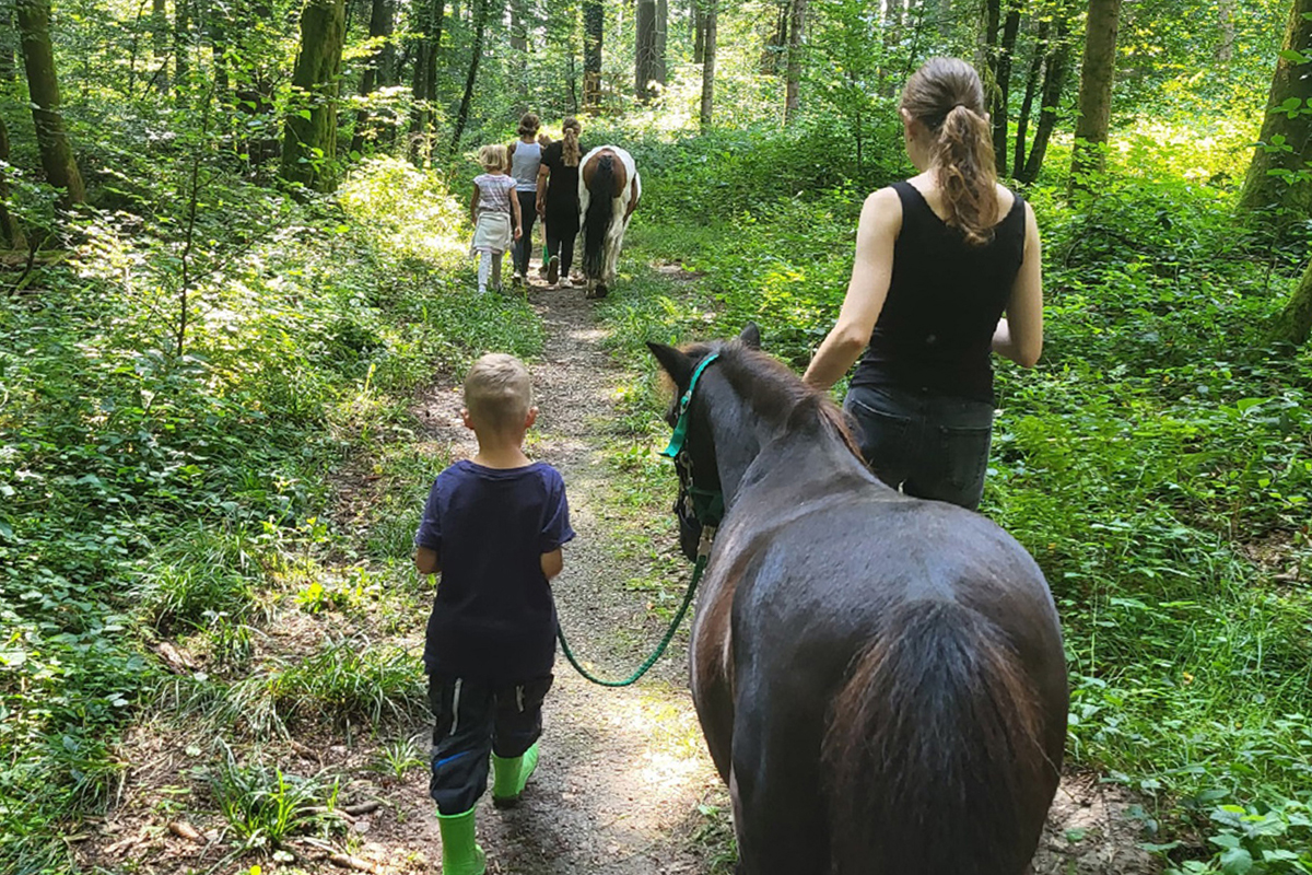 Kinder und Betreuerinnen führen Pferde durch den Wald.