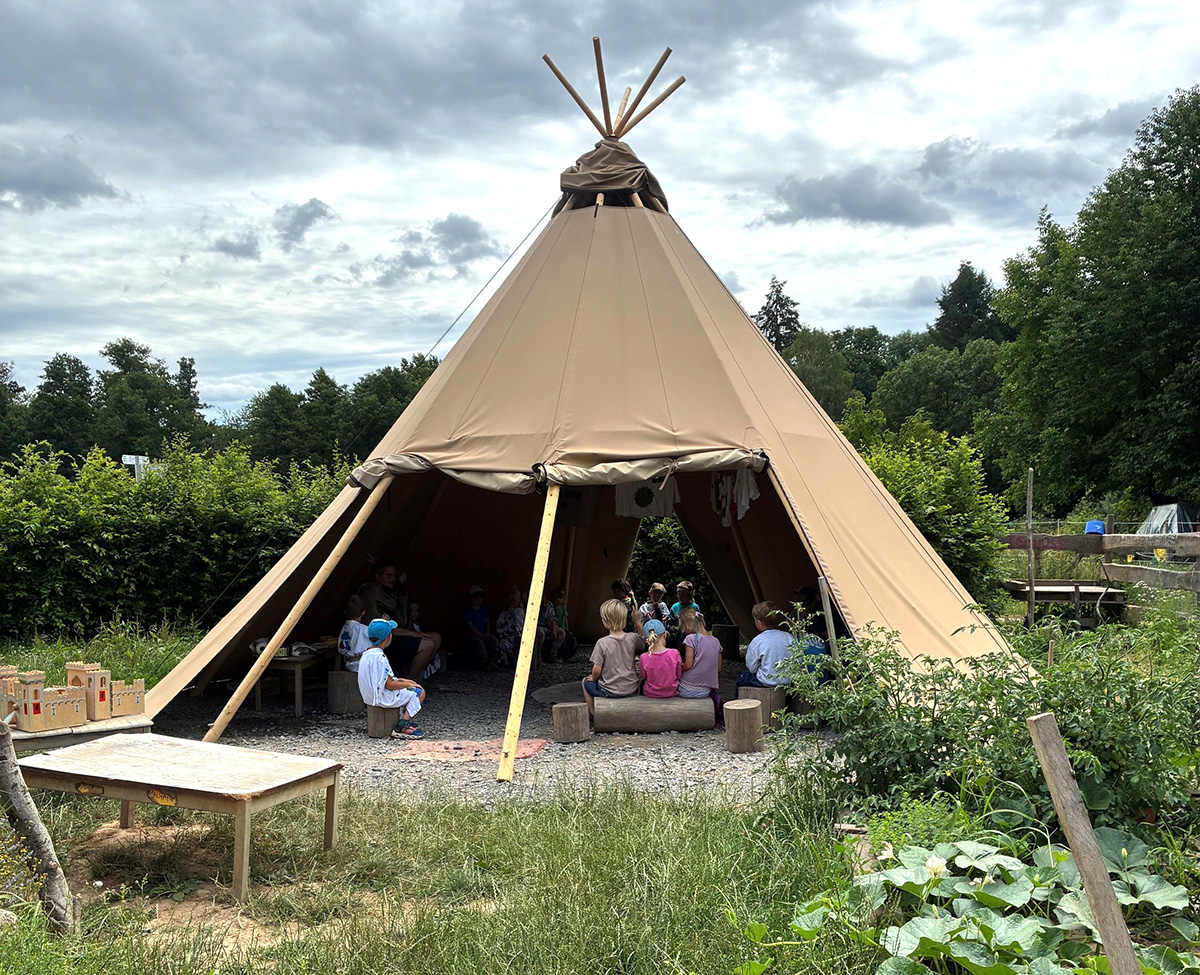 Kinder sitzen im halb geöffneten Tipi des Naturkindergartens Wald- und Wiesenwichtel