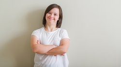 Down syndrome woman standing over wall happy face smiling with crossed arms looking at the camera. Positive person.