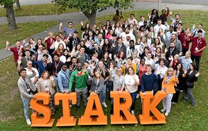 Eine Gruppe von etwa 80 Personen steht hinter großen Buchstaben mit dem Schriftzug "Stark" und winkt in die Kamera