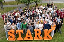 Eine Gruppe von etwa 80 Personen steht hinter großen Buchstaben mit dem Schriftzug "Stark" und winkt in die Kamera