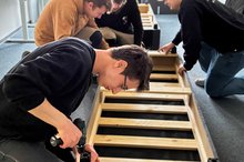 Auszubildende der Firma Mosca bauen mit Auszubildenden des Berufsbildungswerks Mosbach-Heidelberg in einem Zimmer Möbel zusammen.