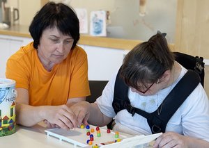 Eine Frau spielt mit einer Klientin mit Behinderung ein Brettspiel.