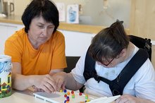 Eine Frau spielt mit einer Klientin mit Behinderung ein Brettspiel.