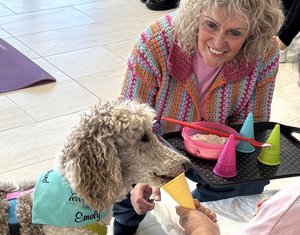 Karin Bäder kniet neben ihrem Besuchshund, Großpudel Emely, im Seniorenzentrum Mosbach