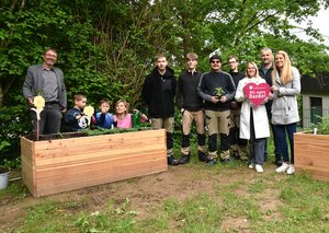 Menschen aus der Johannes-Diakonie stehen im Garten des Schulkindergartens Kleckse zwischen zwei neuen Hochbeeten.
