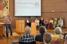Lotsen und Lotsinnen vom Maria-Zeitler-Pfad stehen und sitzen auf der Bühne in der Johanneskirche