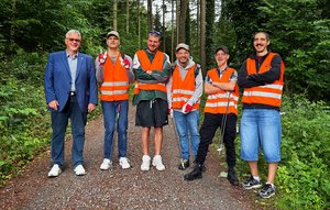Bürgermeister Mathias Haas und eine Gruppe ehrenamtlicher Müllsammler aus der Johannes-Diakonie stehen auf einem Waldweg.