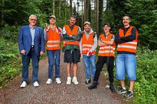 Bürgermeister Mathias Haas und eine Gruppe ehrenamtlicher Müllsammler aus der Johannes-Diakonie stehen auf einem Waldweg.