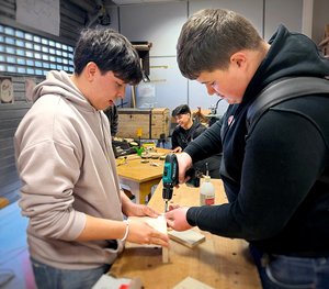 Zwei Auszubildende arbeiten an einer Holz-Werkbank.