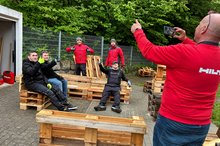 Ein Hilti-Mitarbeiter macht Fotos von Kollegen und Schülern, die auf Palettenmöbeln sitzen.