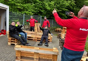 Ein Hilti-Mitarbeiter macht Fotos von Kollegen und Schülern, die auf Palettenmöbeln sitzen.