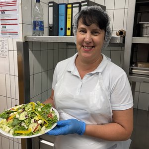 Eine Frau hat einen Teller mit Salat in der Hand und lächelt in die Kamera.
