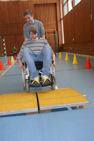 Zwei Jugendliche, einer im Rollstuhl, einer, der den Rollstuhl schiebt.