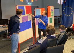 Vortragende stehen an einer Pinnwand vor Auszubildenden 