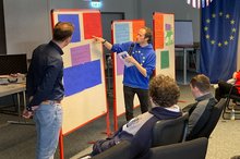 Vortragende stehen an einer Pinnwand vor Auszubildenden 