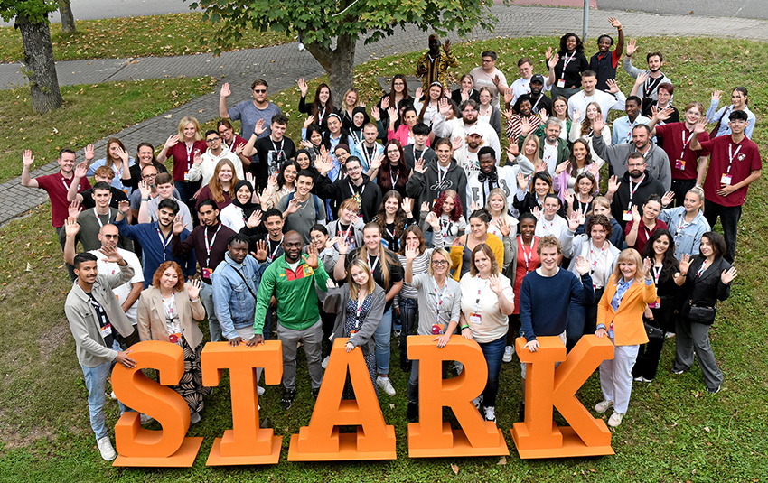 Eine Gruppe von etwa 80 Personen steht hinter großen Buchstaben mit dem Schriftzug "Stark" und winkt in die Kamera